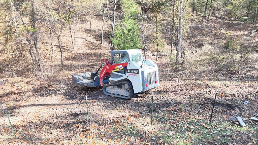 Compact track loader with forestry mulcher clearing brush and trees on a hillside property – Hood Lawn Care and Services
