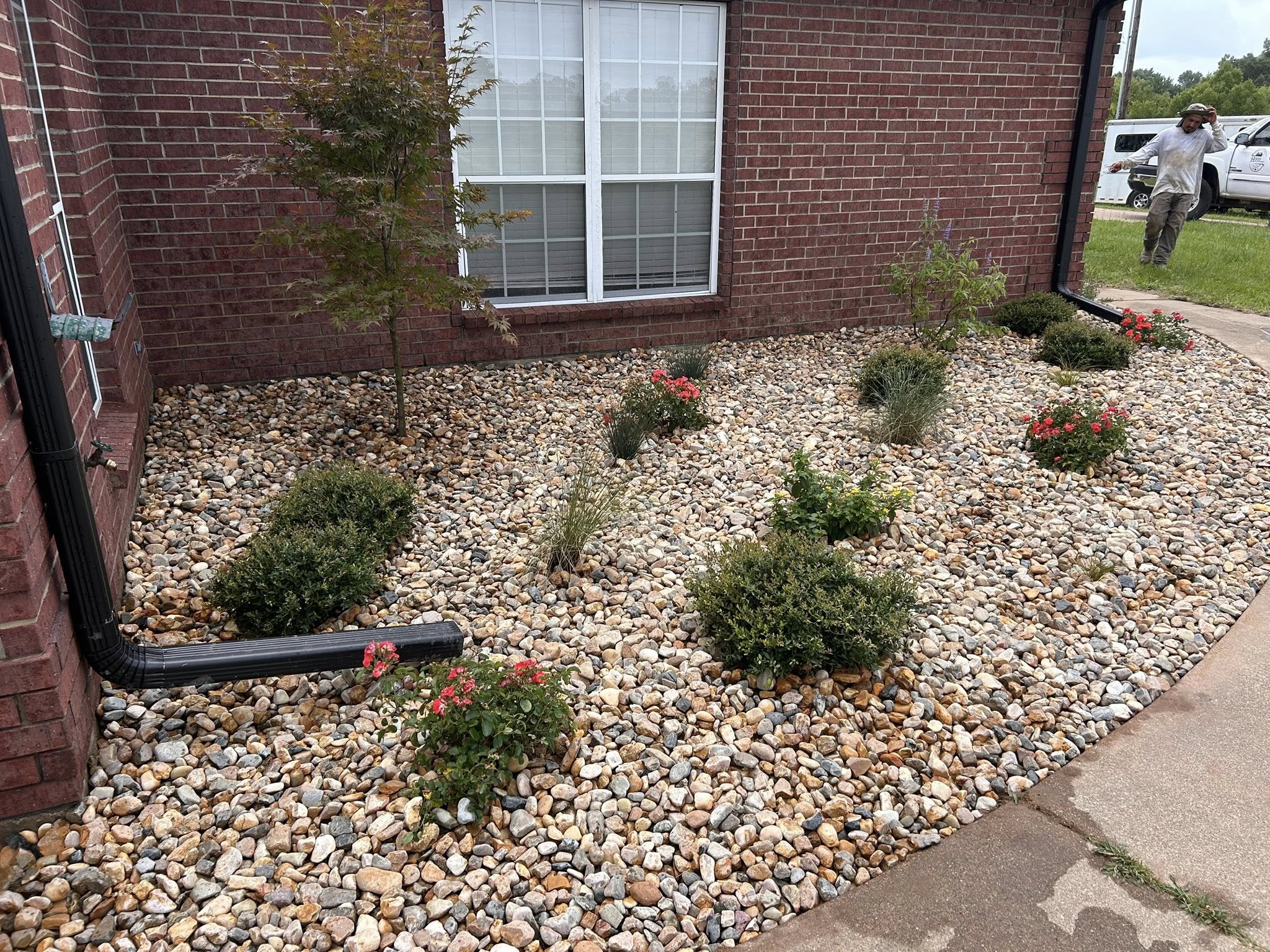 Front yard landscaping with decorative river rock, shrubs, and blooming flowers along a red brick home – Hood Lawn Care and Services