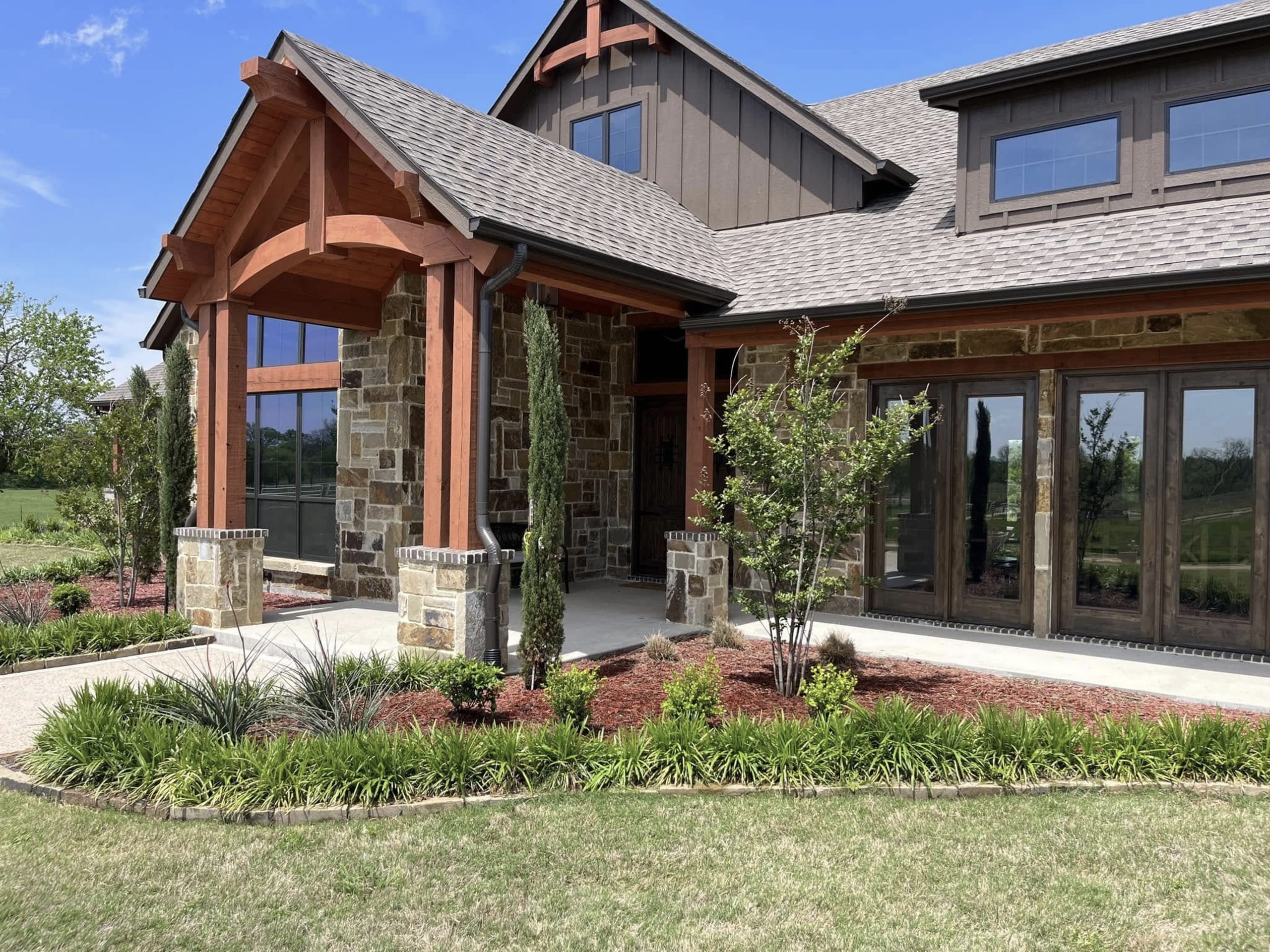 Modern residential landscape with stone home, walkway, and fresh mulch bed designed by Hood Lawn Care