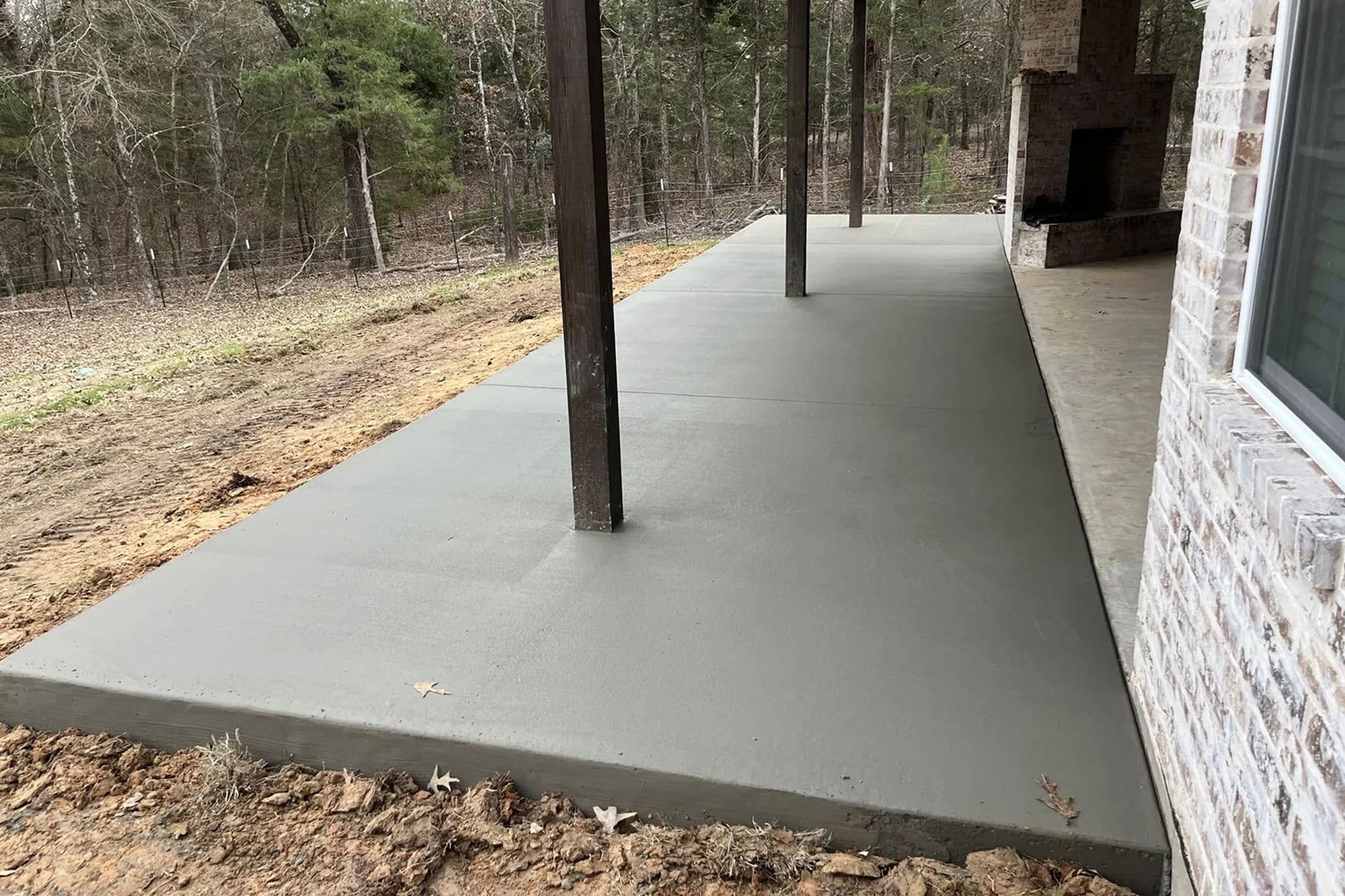 Newly poured concrete patio with smooth finish under covered porch, ideal for outdoor living – Hood Lawn Care and Services.